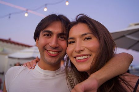 Two people smiling closely together at an evening event with string lights in the background.