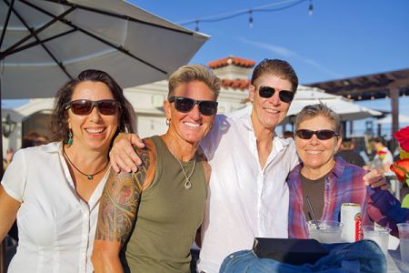 Four friends wearing sunglasses sitting together outdoors at a sunny rooftop gathering.