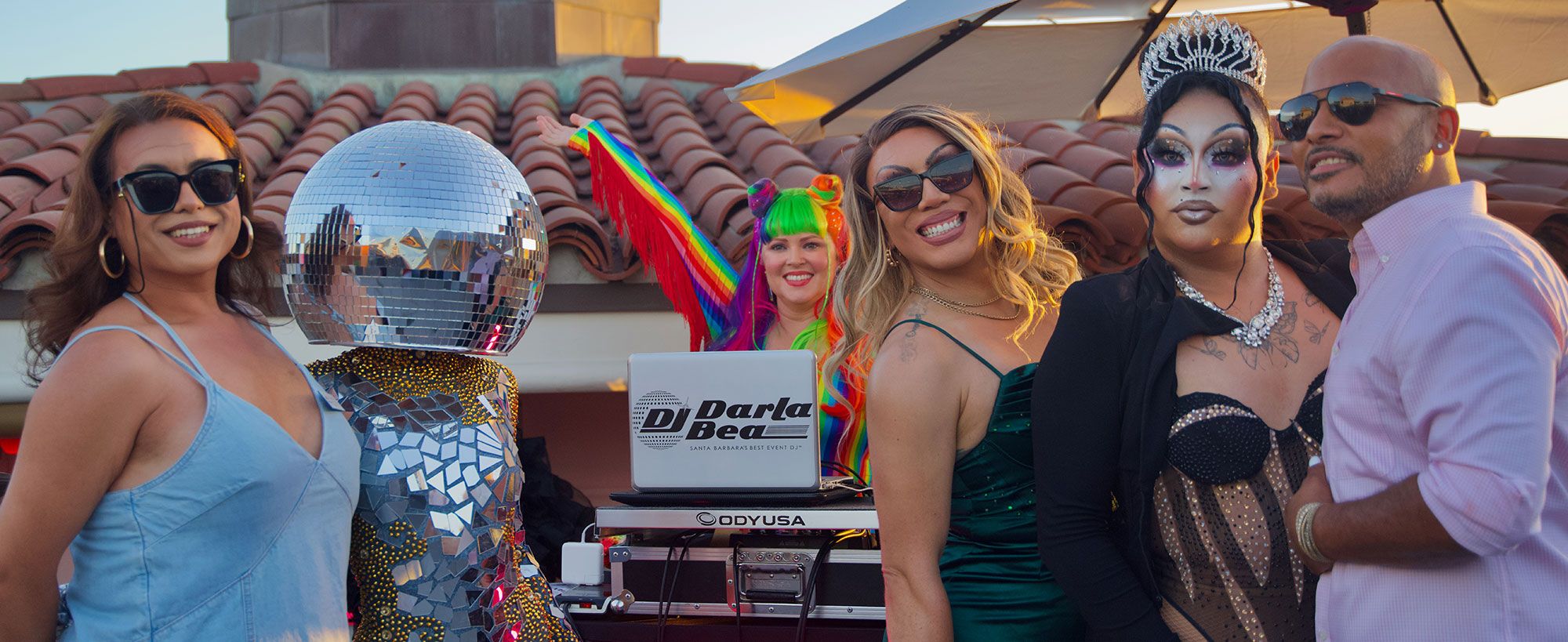 Group of people posing at the Canary rooftop mixer event with a DJ, disco ball costume, and festive outfits.