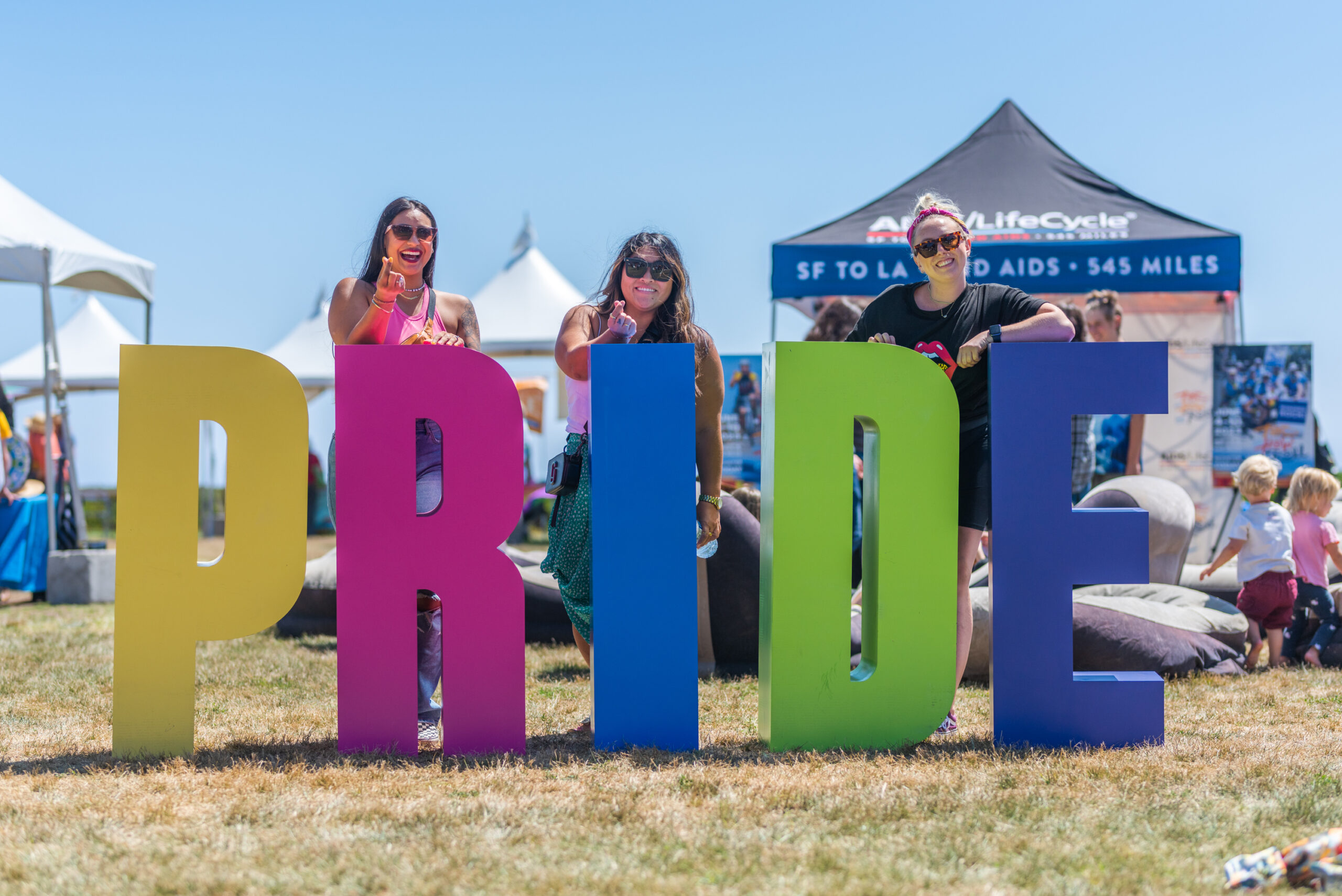 Three people in front of big block letters spelling out "PRIDE"